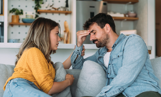 Young couple discussing a serious issue, man looks tired, sitting on a sofa, in a house.